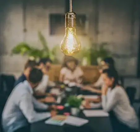 Lightbulb with team gathered around a table in the background